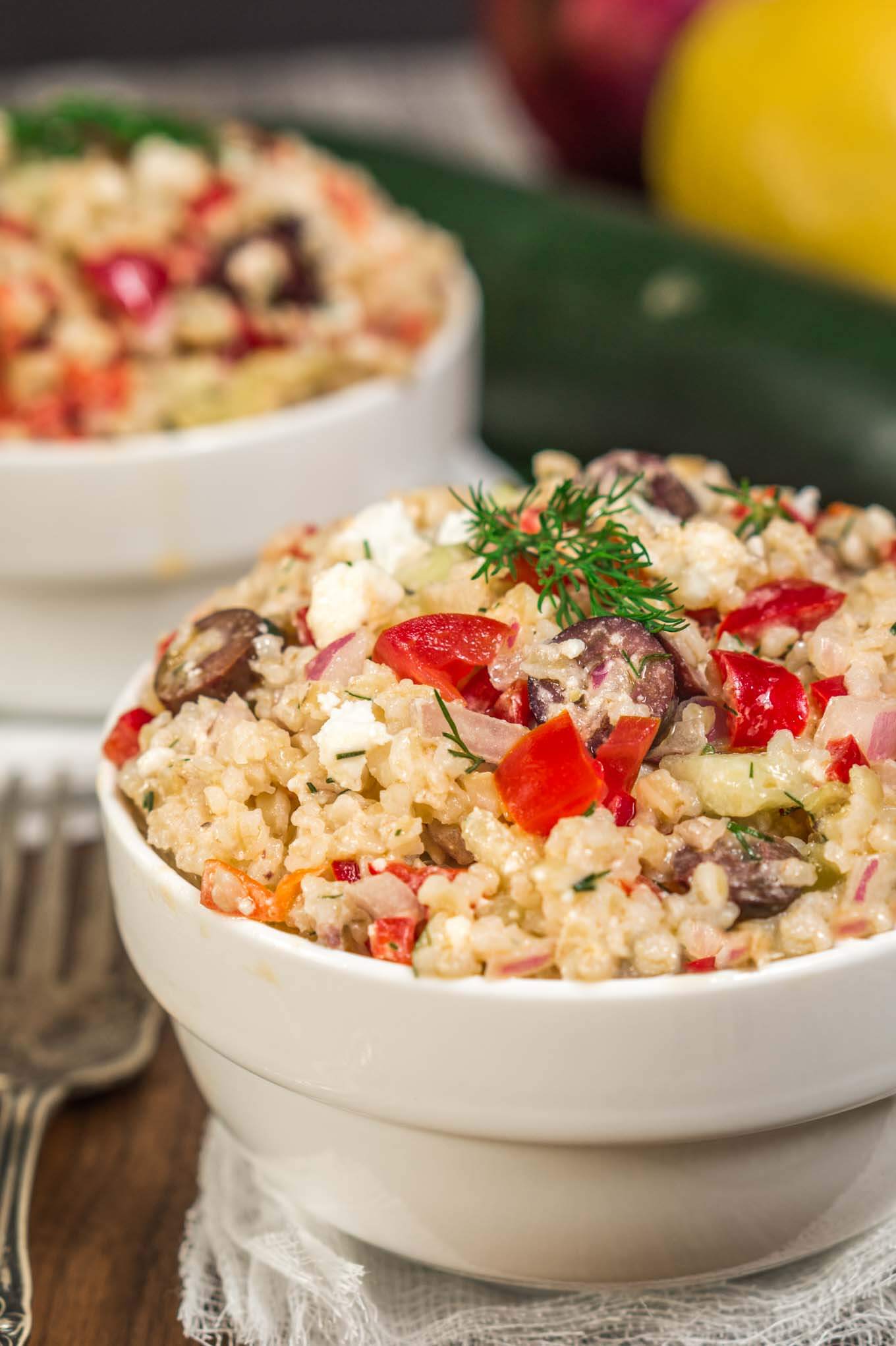 White bowl of Tabouli salad topped with diced red pepper, Feta Cheese, and dill. A second bowl sits in the background.
