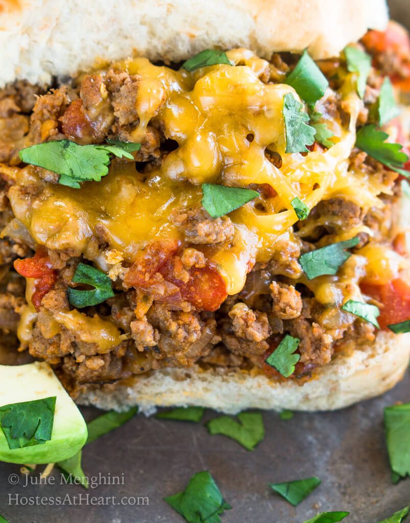 A bun topped with ground taco beef filling, melted cheese, and chopped cilantro.