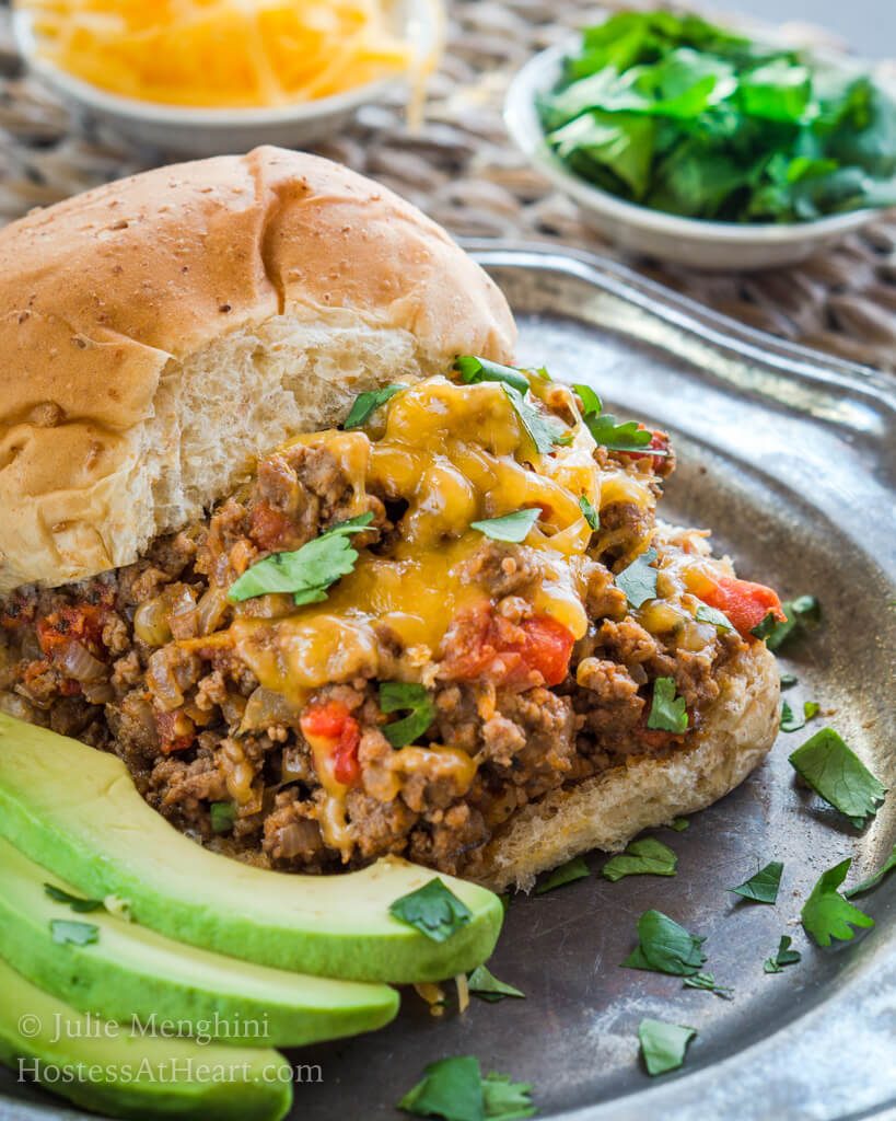 A Mexican Sloppy Joe sitting open faced on a plate topped with cilantro and slices of avocado. Hostess At Heart