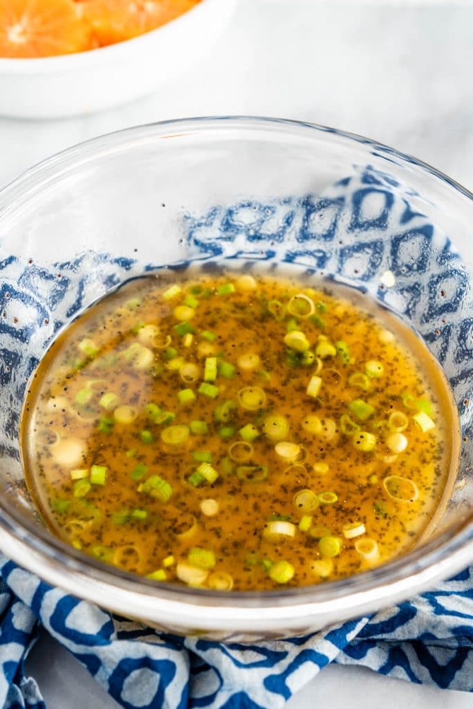 A glass bowl of poppyseed vinaigrette sitting on a blue checked napkin.