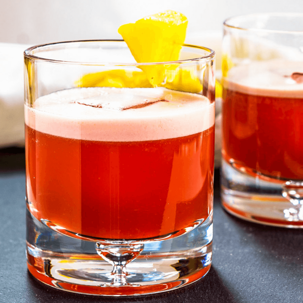 Closeup Sideview of two rocks glasses filled with a Campari Drink and garnished with pineapple.
