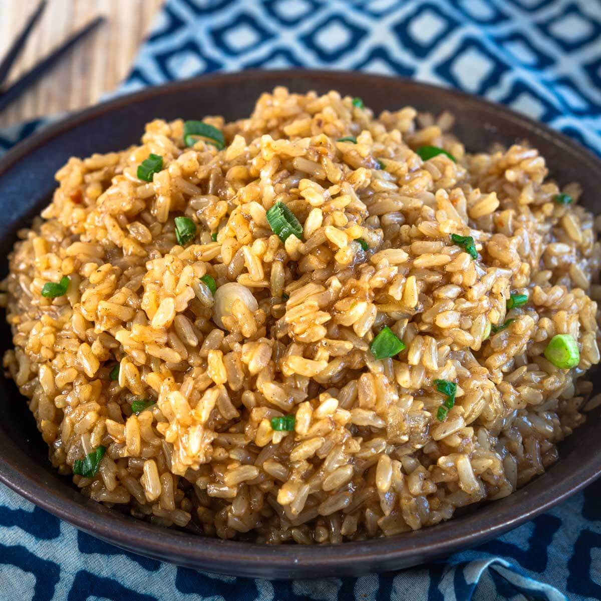 3/4 view of a black bowl of saucy brown rice garnished with green onion