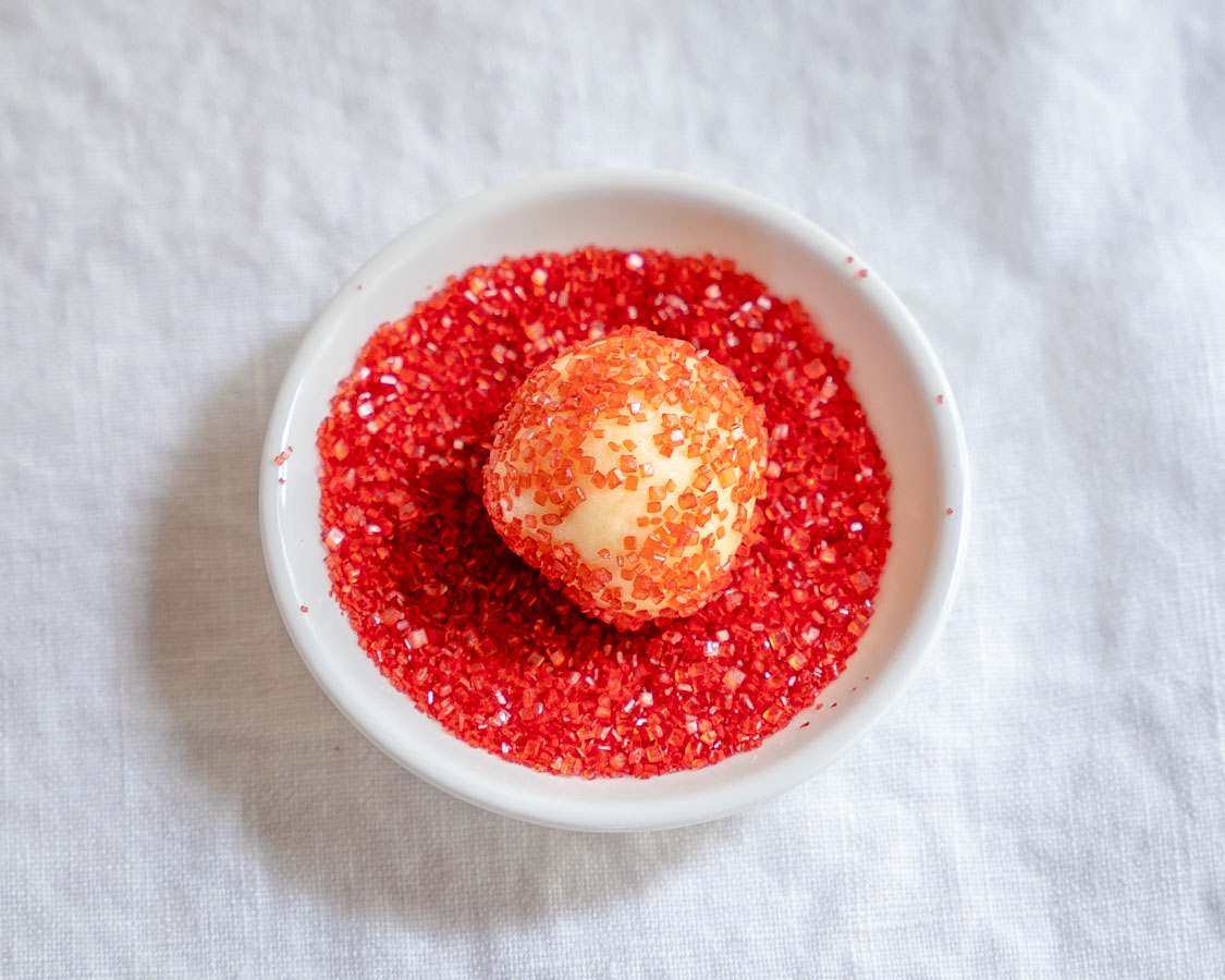 A scoop of butter cookie dough rolled in red sprinkles in a bowl - Hostess At Heart