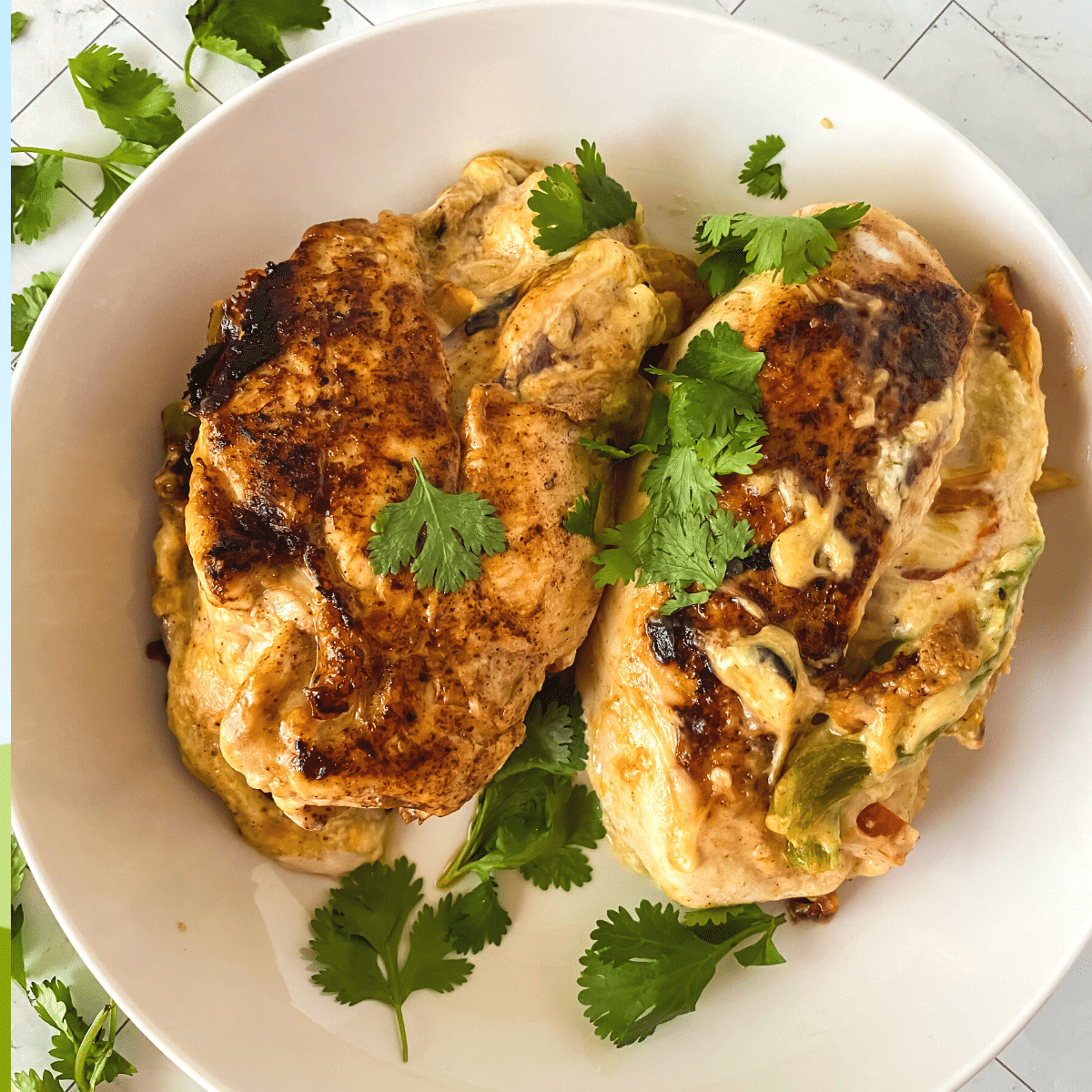 Top down image of two cooked chicken breasts with cheese and peppers over the top and garnished with cilantro.