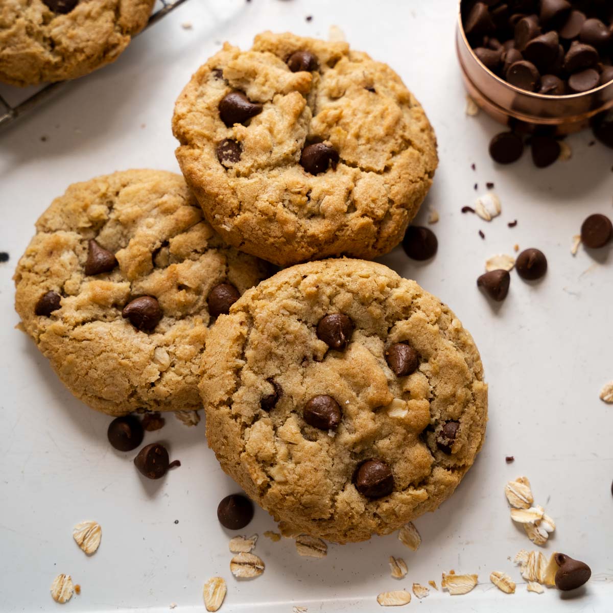 Top down photo of three chocolate chip oatmeal cookies sitting around scattered chocolate chips and oats.