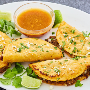 Beef Birria Tacos sitting on a plate garnished with chopped cilantro and cheese - Hostess At Heart