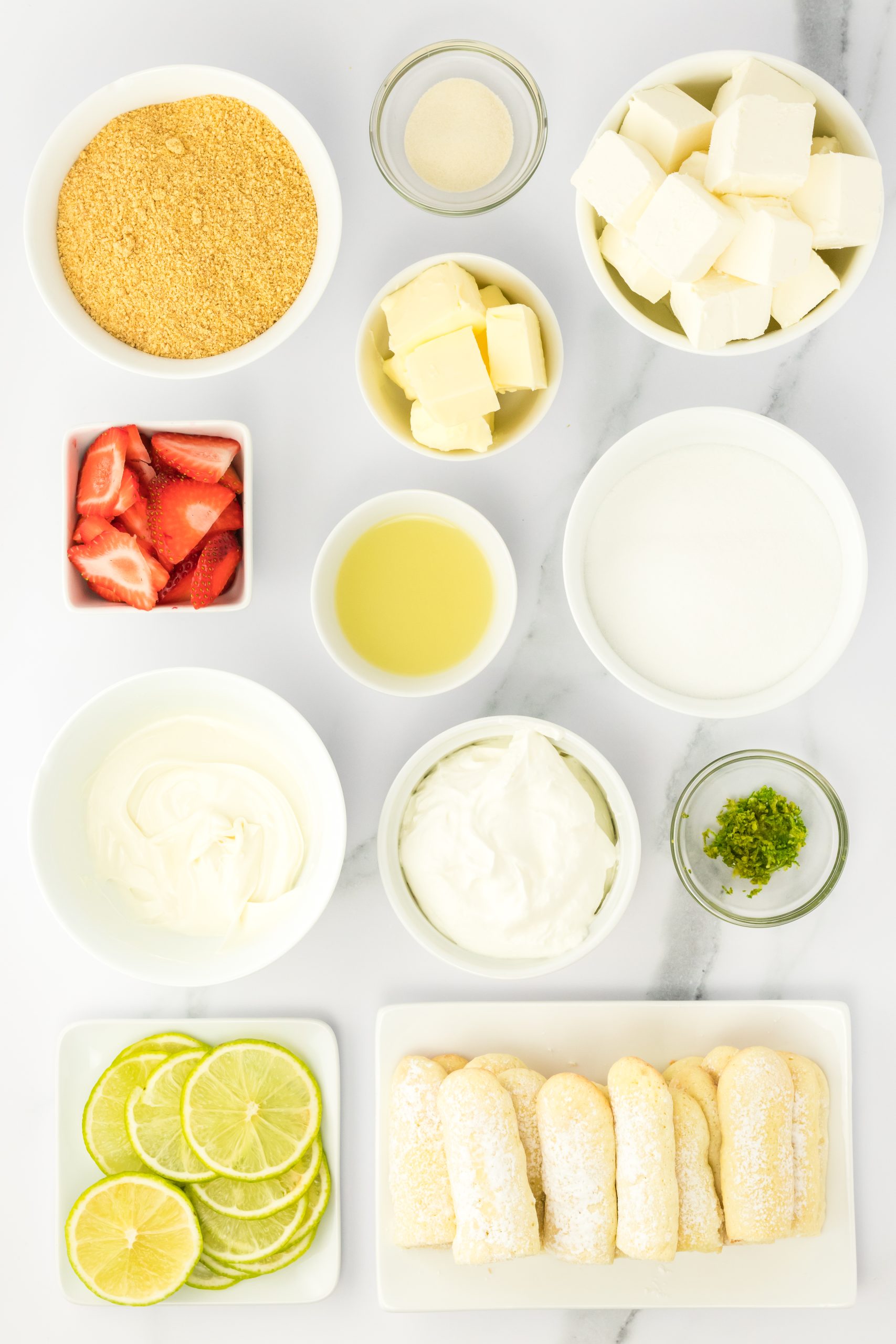 Ingredients for unbaked lime cheesecake recipe: graham cracker crumbs, butter, sugar, cream cheese, strawberries, gelatin, lime juice, whipped cream, white baking chocolate, lime zest, lady fingers, sliced lime, and sliced strawberries.