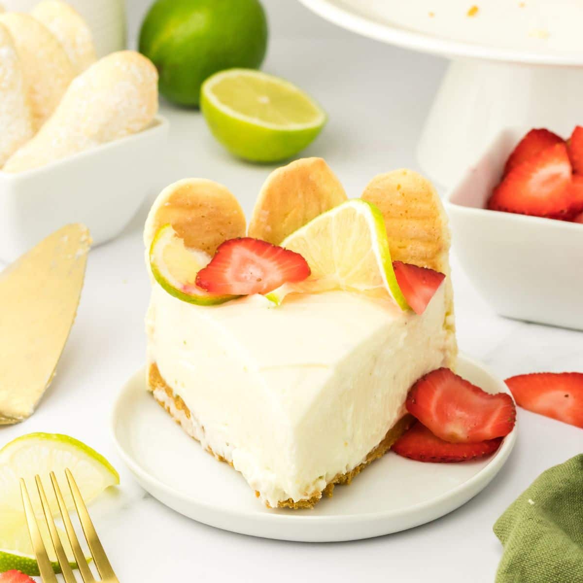 Front view of a slice of lime cheesecake with a graham cracker crust topped with slices of fresh strawberries and lime wheels. Hostess At Heart